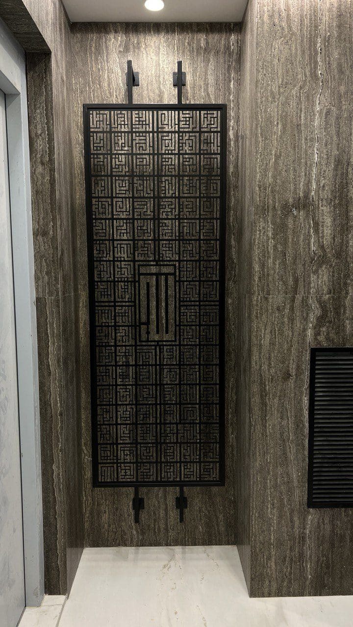 Laser-cut Islamic calligraphy panel mounted on a stone wall